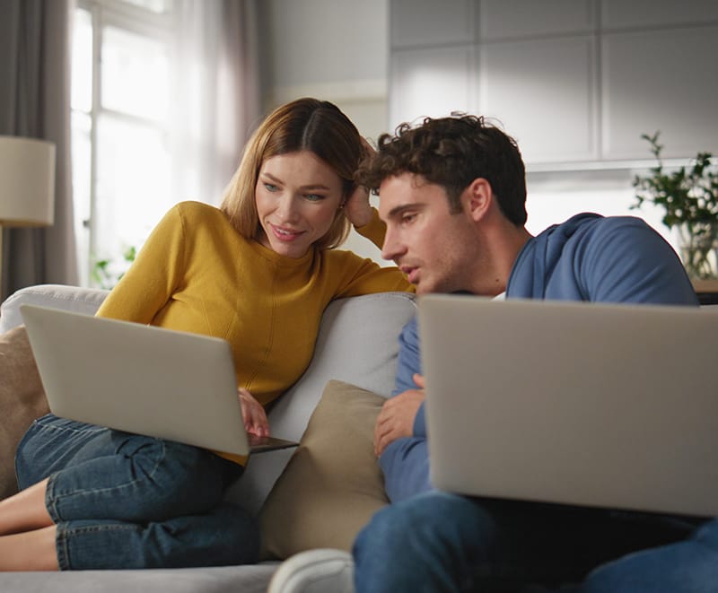 Ein Mann und eine Frau besprechen etwas an Laptops auf einer Couch